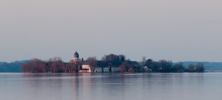 Kleine Insel mit Bäumen und einer weißen Gebäude-Silhouette im ruhigen Chiemsee.